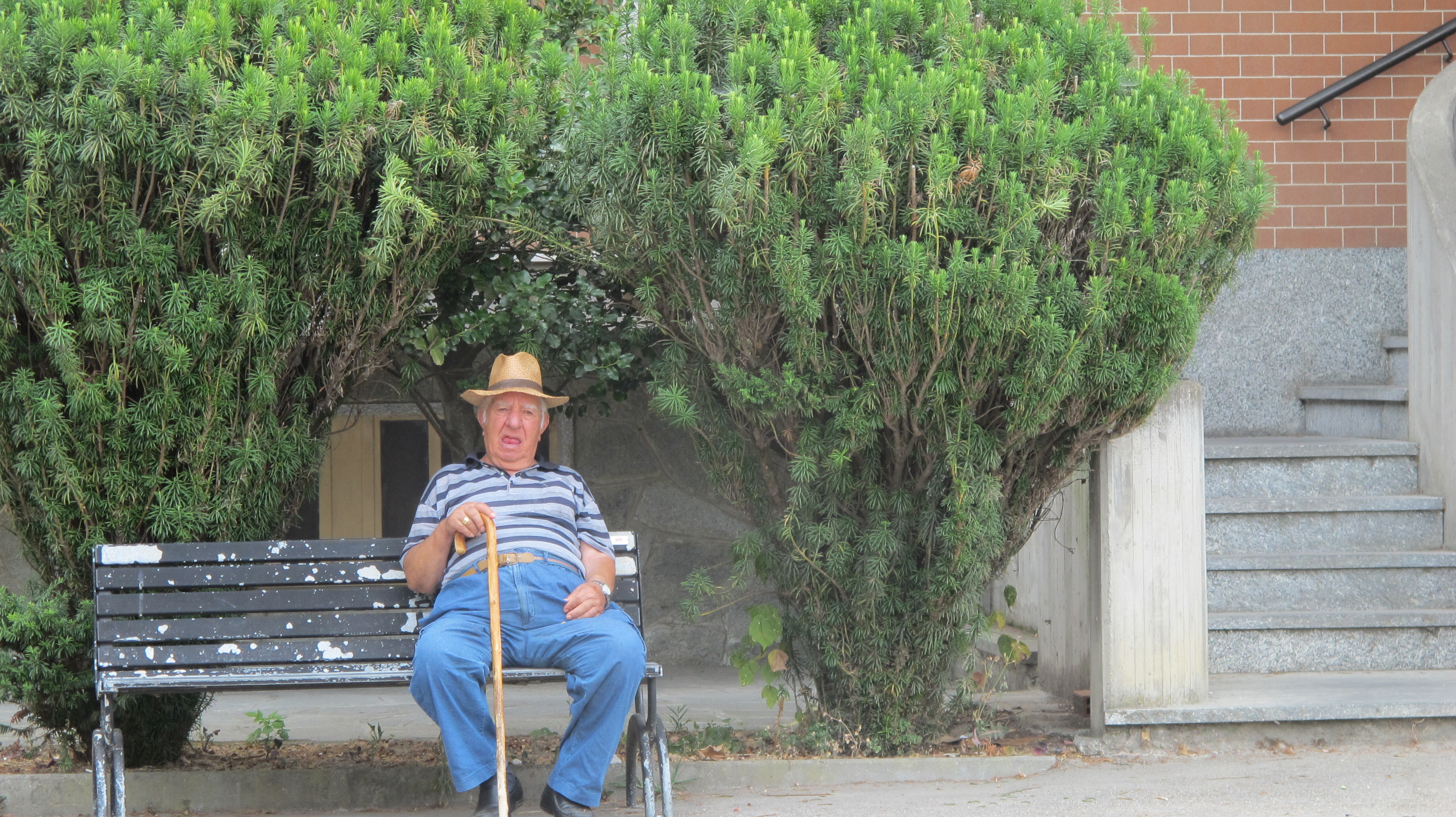 The old farmer watches over his small village from a bench near the bank as I go over to the butcher for meat. 